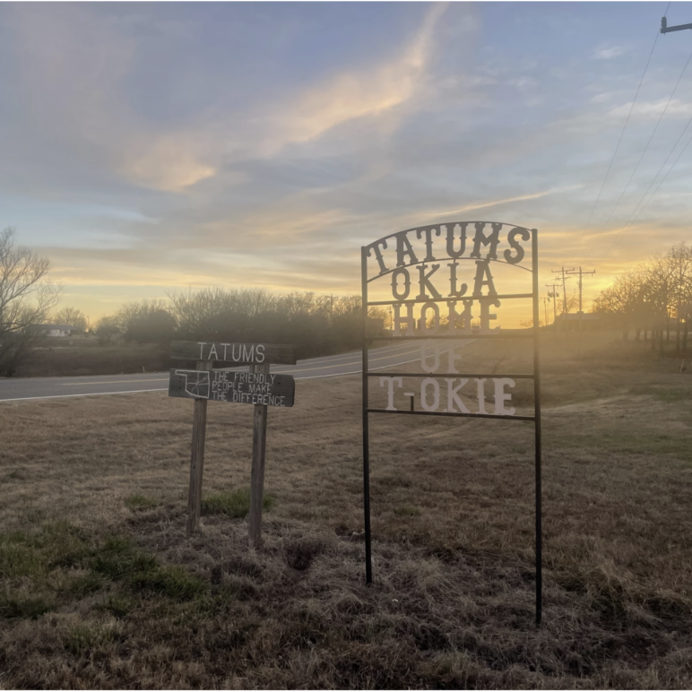 Two road signs in Tatums, Oklahoma. One reads "TATUMS: The friendly people make the difference," and the other "Tatums, Okla: Home of T-Okie."